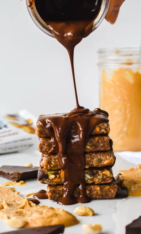 Rich melted chocolate being poured over a stack of YES Bar Peanut Butter Dark Chocolate cookie bars.