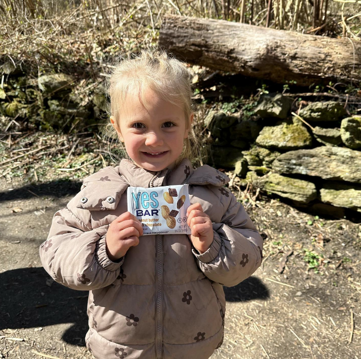 Child outdoors smiling while holding a Peanut Butter Dark Chocolate YES Bar.
