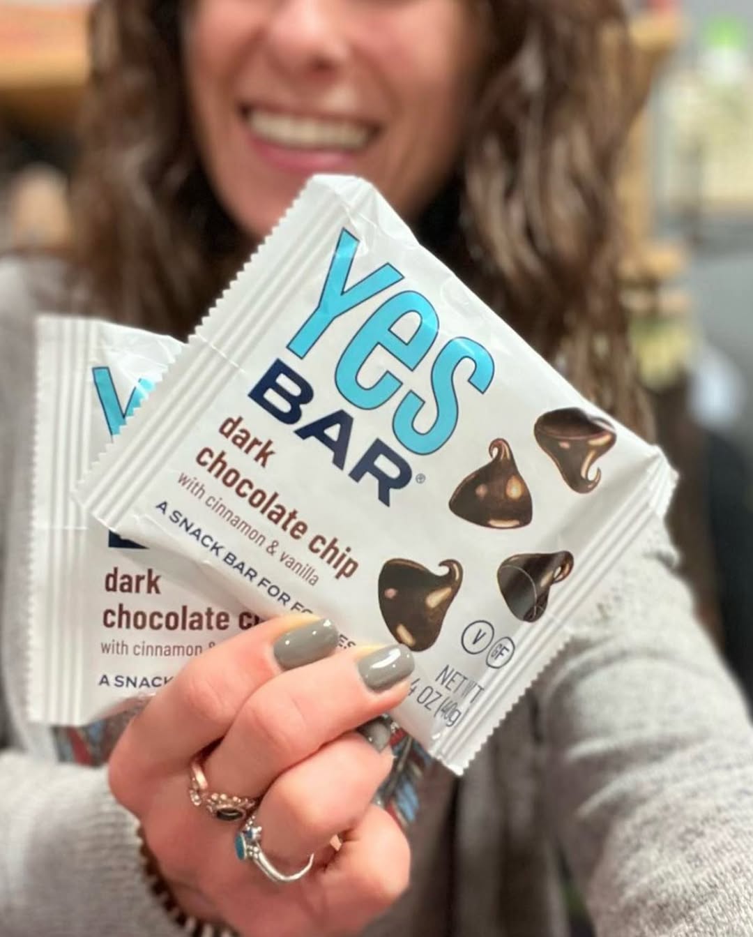 A woman holding two packets of YES Bar’s dark chocolate chip with cinnamon & vanilla snack bars.