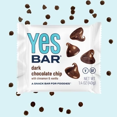A pack of “YES Bar” dark chocolate chip cookie bar with scattered chocolate chips around it.
