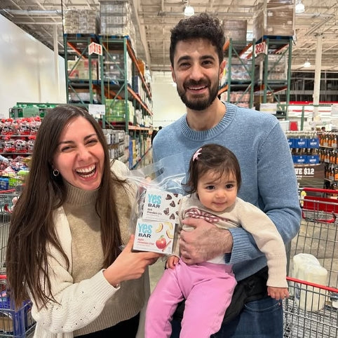 A family holding different YES Bar flavors in a supermarket aisle.