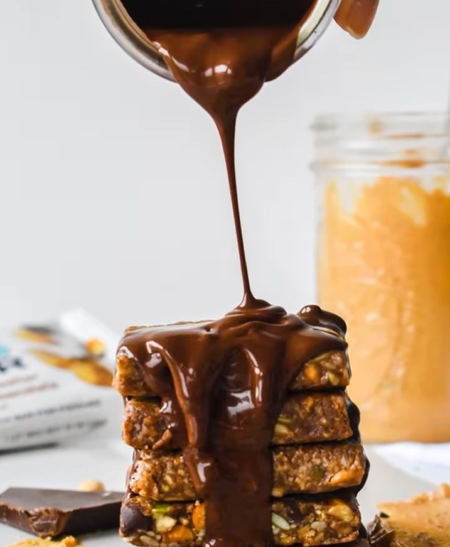 Rich melted chocolate being poured over a stack of YES Bar Peanut Butter Dark Chocolate cookie bars.