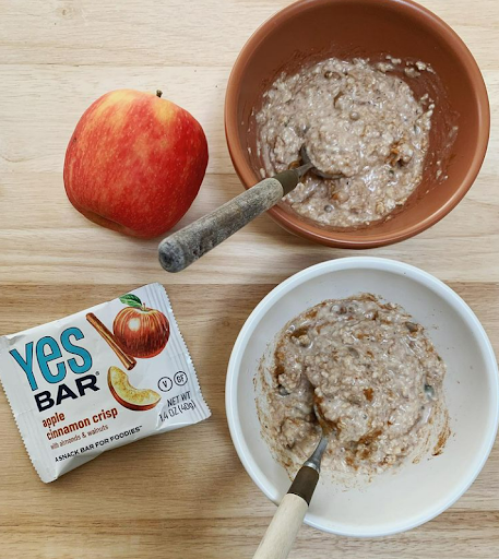 Apple cinnamon overnight oats, an apple, and a YES Bar snack bar arranged in a flat lay.